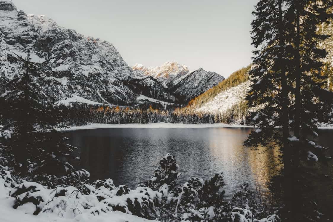 Lac paisible entouré de montagnes enneigées et de forêts.